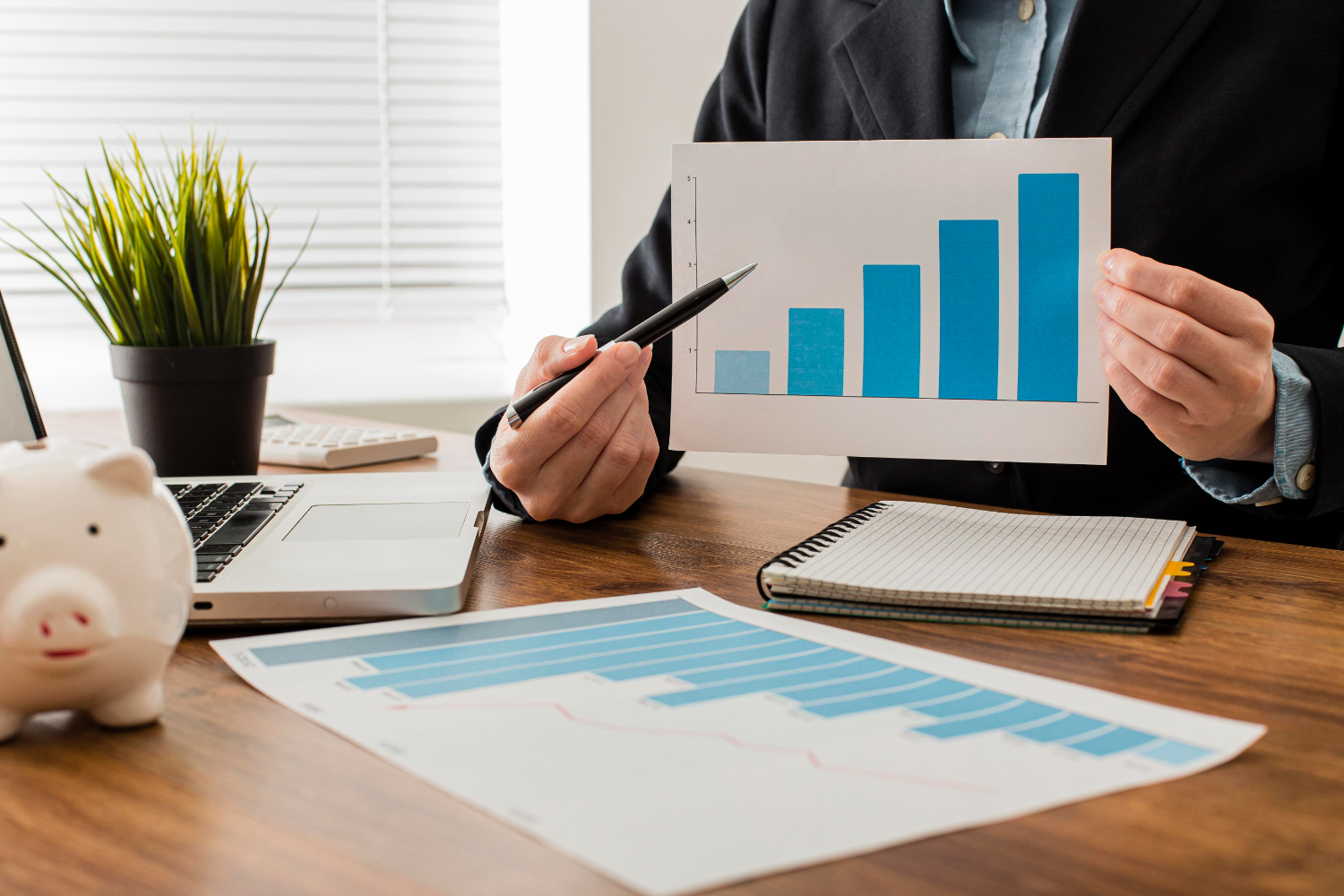 Un homme en costume analysant un graphique financier de barres représentant le free cash flow, avec un ordinateur portable et une tirelire sur le bureau.